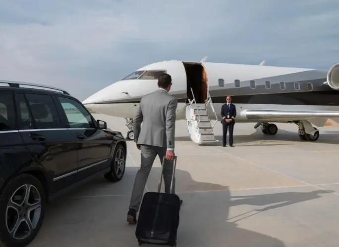 Business executive with luggage walking toward a private jet on the tarmac, greeted by crew, for a corporate charter flight