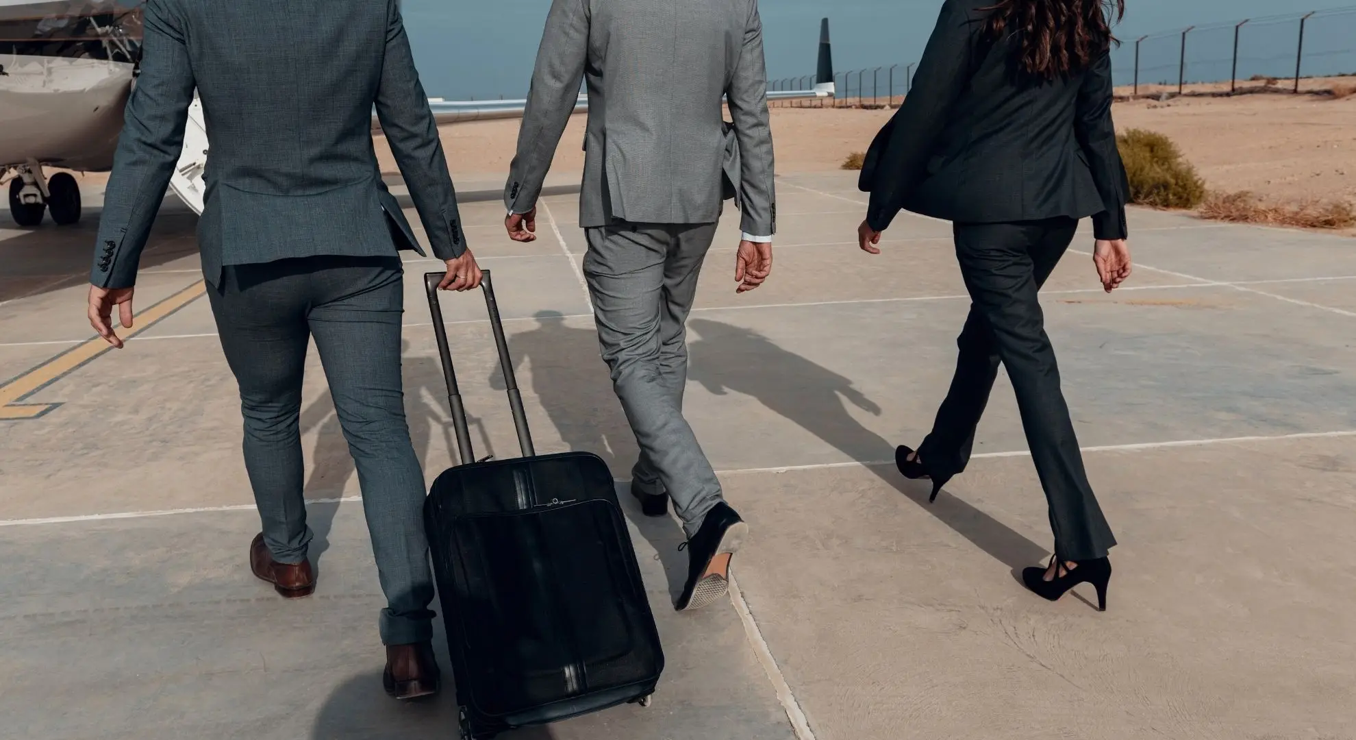 Business executives in suits walking across tarmac toward a private jet for a corporate charter flight in Indonesia