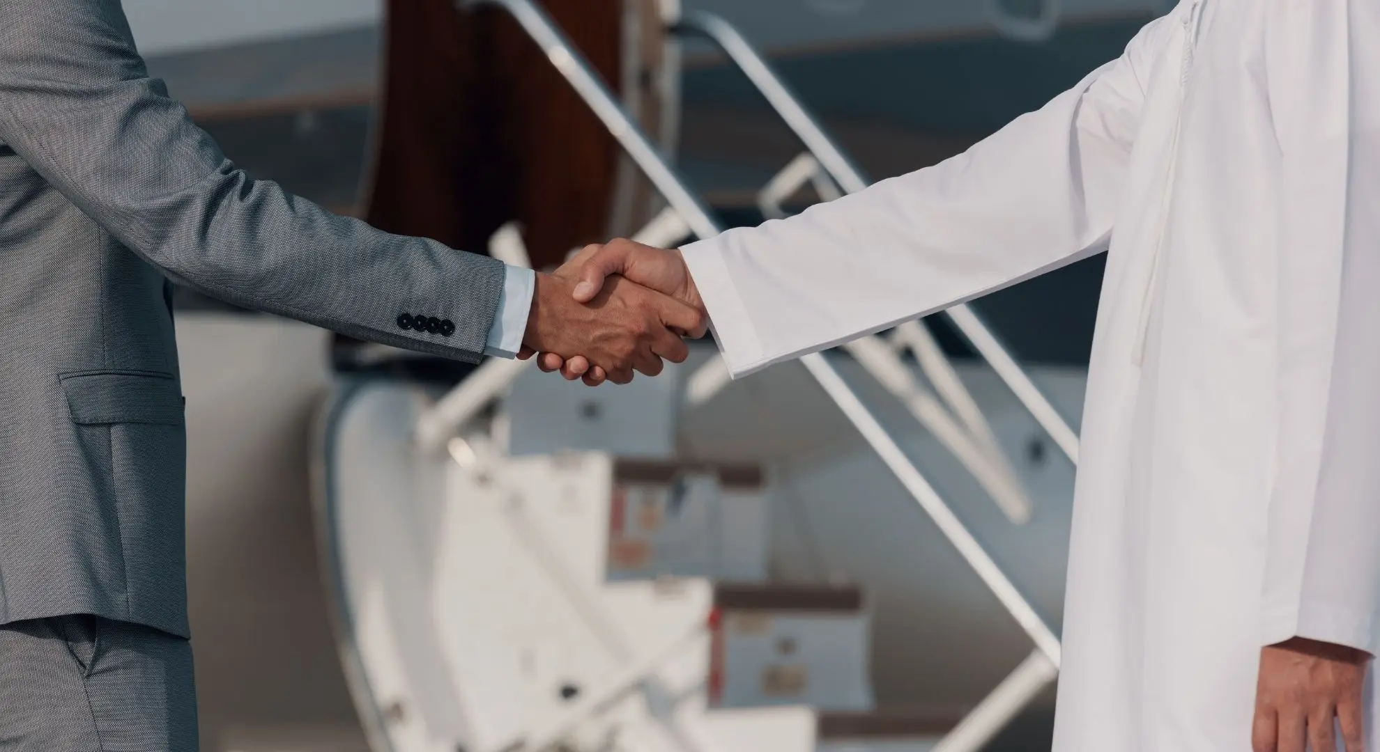 Business executives shaking hands beside a private jet stairway in Indonesia