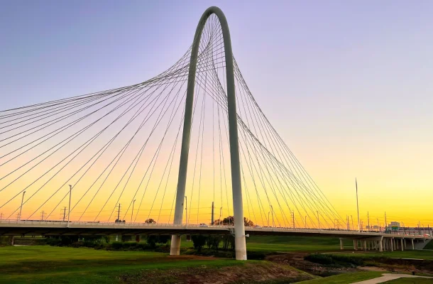 Modern cable-stayed bridge with twin arches spanning across Dallas skyline during golden sunset