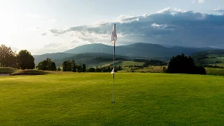 Pristine golf course with flagstick on manicured green fairway, mountain ranges visible in distance
