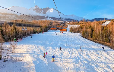 Snow-covered ski slopes with chairlift and skiers at Aspen mountain resort under clear blue skies