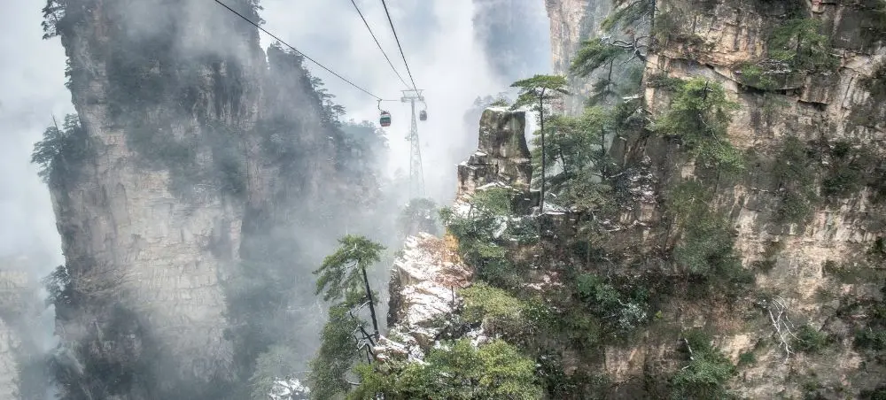 Cable car ascending through misty sandstone pillars and lush vegetation in China's dramatic mountain landscape