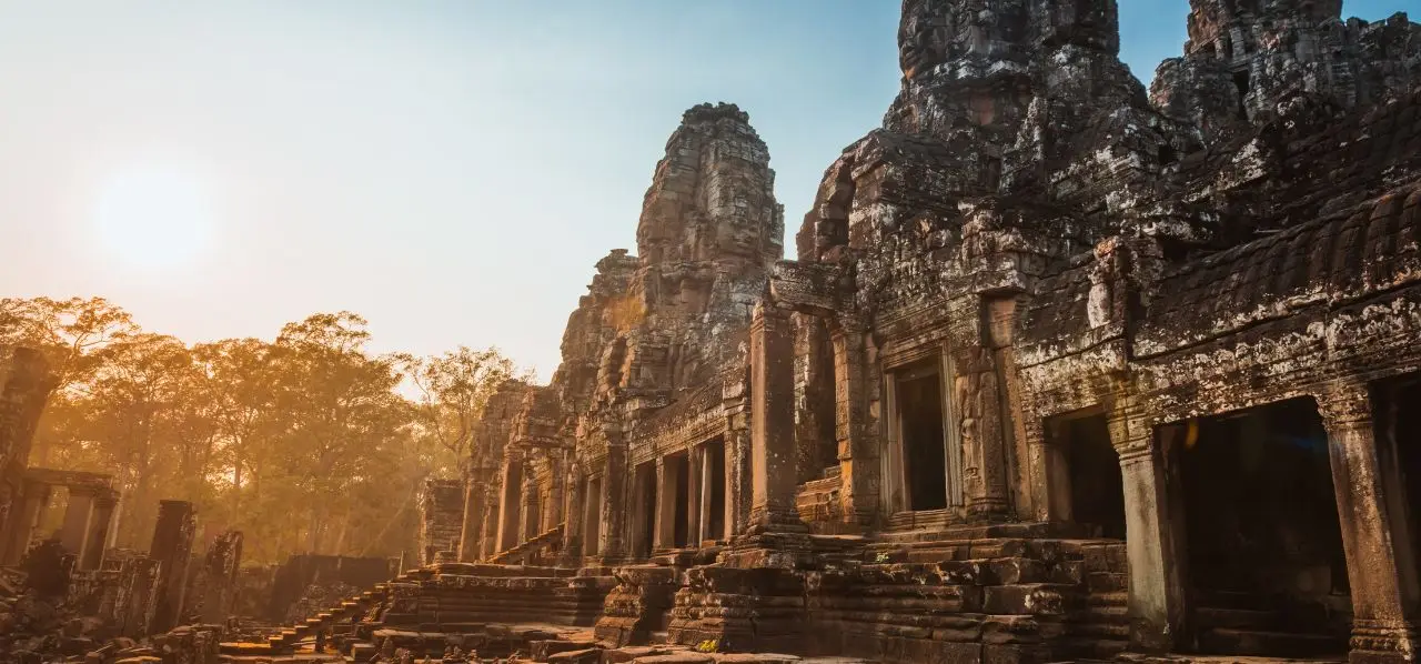 Ancient Angkor Wat temple complex in Cambodia bathed in golden sunrise light through tropical trees