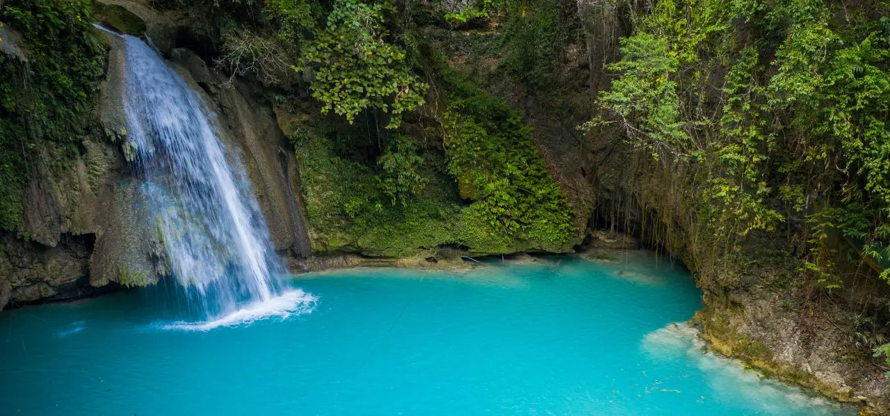 Stunning turquoise waterfall pool surrounded by lush tropical rainforest in Cebu, Philippines