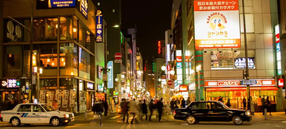 Bustling Fukuoka street at night with illuminated Japanese signs, restaurants, and pedestrians exploring the vibrant city