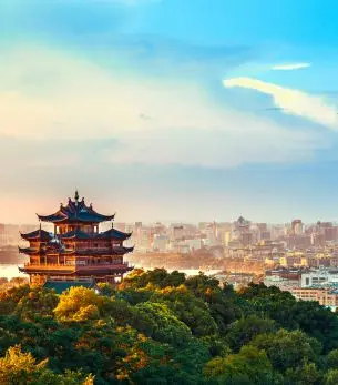 Traditional pagoda overlooking Hangzhou cityscape at sunset with lush green hills and modern skyline