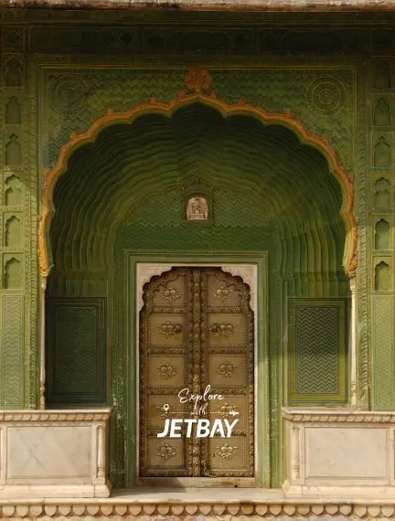 Ornate green Mughal archway with intricate carvings leading to wooden doors in Jaipur's City Palace