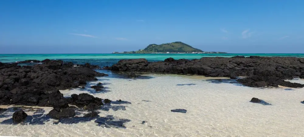 Pristine white sand beach with volcanic rock formations on Jeju Island, showcasing crystal clear turquoise waters