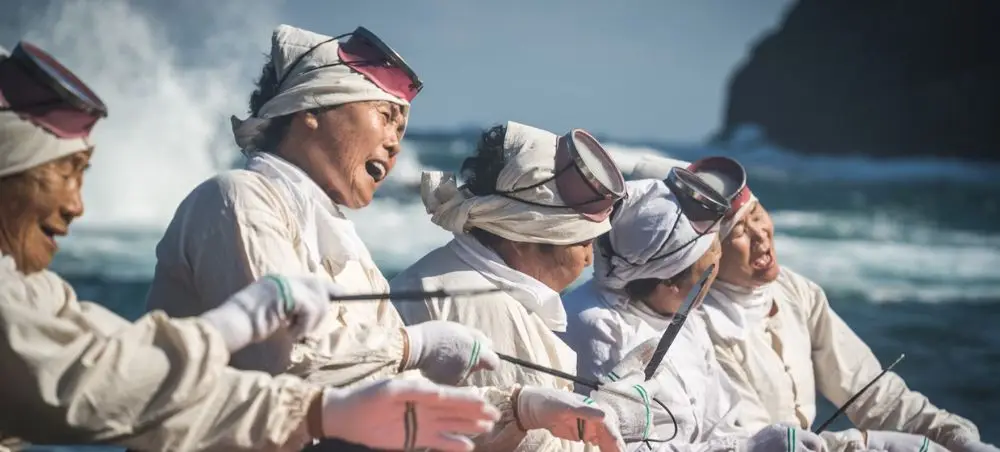 Traditional Jeju Island fishermen in white clothing and headbands working together on their boat near the coast