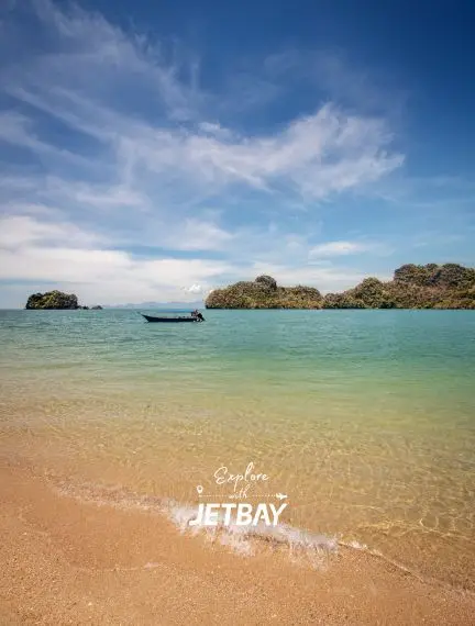 Pristine Langkawi beach with turquoise waters, traditional boat, and lush tropical islands under blue sky