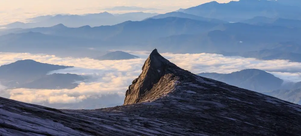 Dramatic mountain peak rising above clouds in Malaysia's highlands during golden hour sunrise