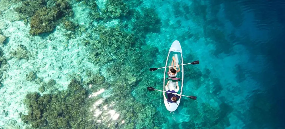 Aerial view of couple kayaking in crystal-clear turquoise waters over coral reefs in the Maldives