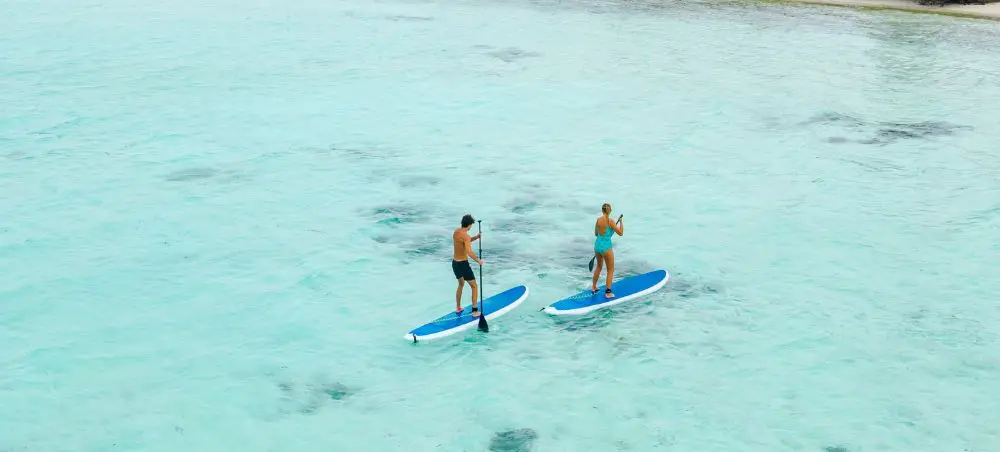 Two travelers paddleboarding on crystal-clear turquoise waters in the Maldives tropical paradise