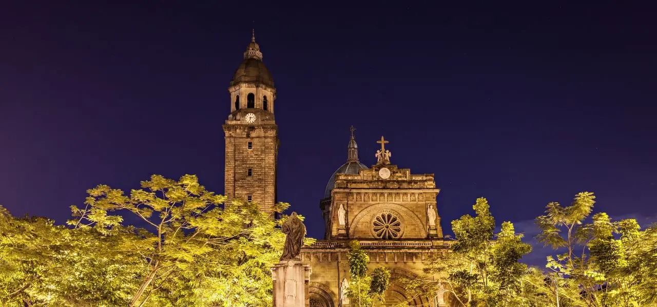 Manila Cathedral's illuminated baroque architecture and bell tower against twilight sky in the Philippines