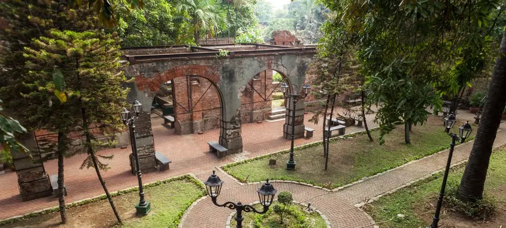 Historic Spanish colonial ruins with brick arches surrounded by lush tropical gardens in Manila, Philippines