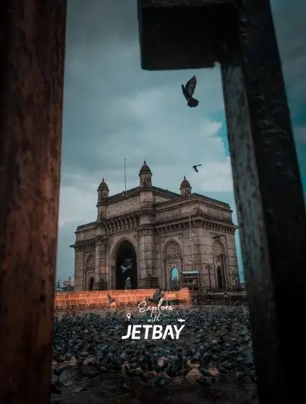 Gateway of India monument in Mumbai framed by stone archway with seagulls flying overhead at dusk