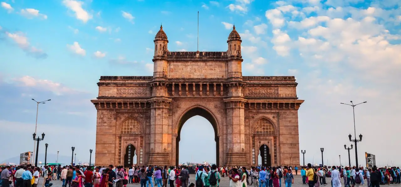 Gateway of India monument in Mumbai with crowds of visitors under dramatic cloudy sky at sunset