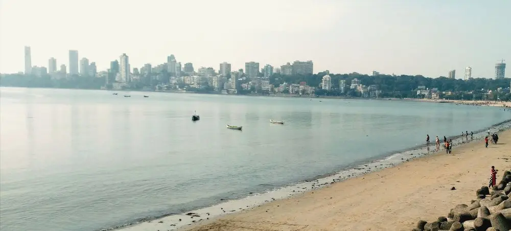 Mumbai's Marine Drive waterfront with city skyline, calm Arabian Sea, and beachgoers enjoying the coastline