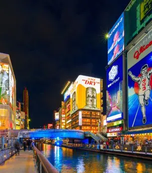 Vibrant neon signs illuminate Dotonbori district canal in Osaka at night, showcasing Japan's iconic urban entertainment quarter
