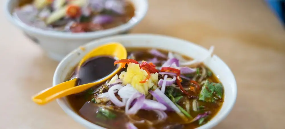 Traditional Penang assam laksa bowls with tamarind broth, fish, vegetables and spicy paste garnish