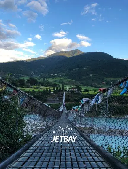Suspension bridge crossing turquoise river in Punakha valley with traditional prayer flags and mountains