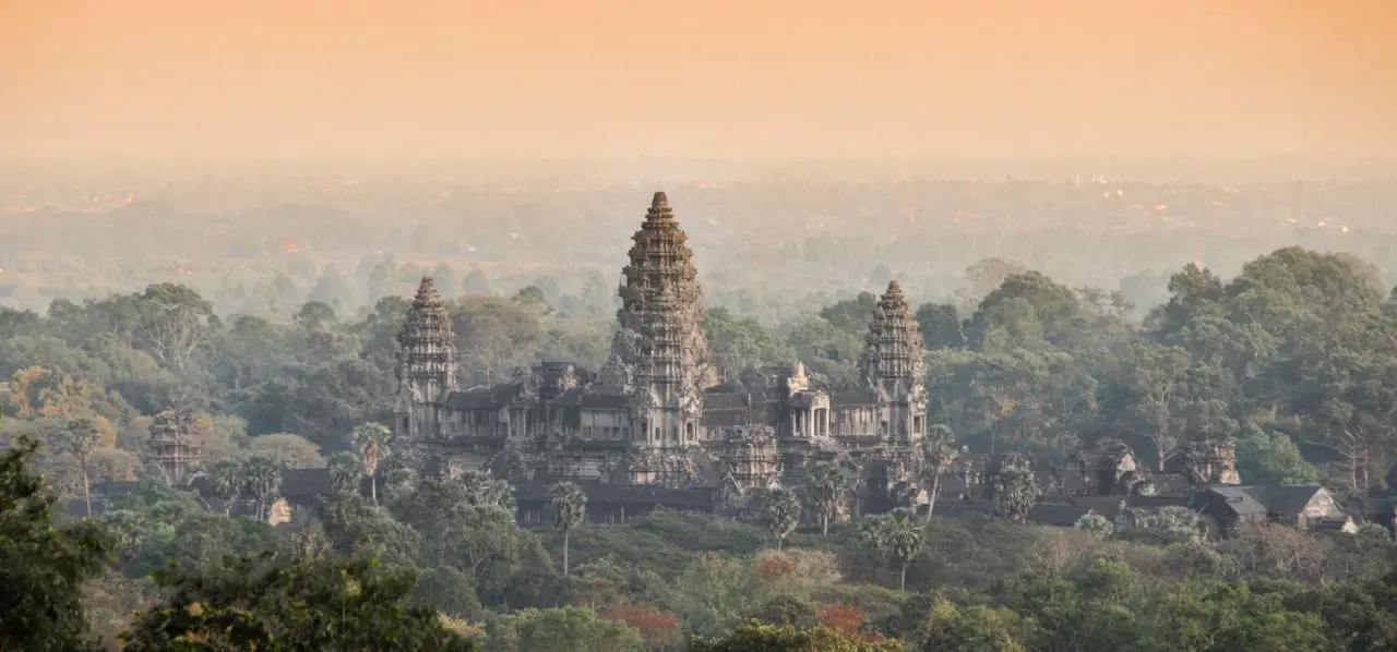 Angkor Wat temple complex rising majestically above lush jungle canopy at golden hour in Siem Reap