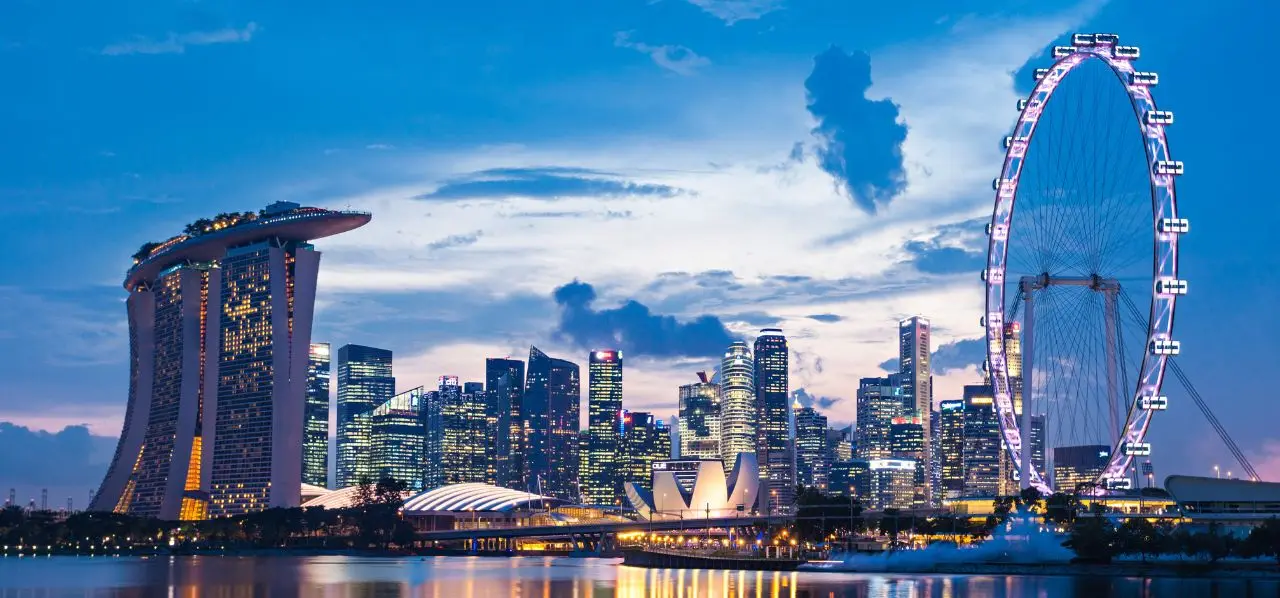 Singapore skyline at dusk featuring Marina Bay Sands, Singapore Flyer, and illuminated skyscrapers reflected in water