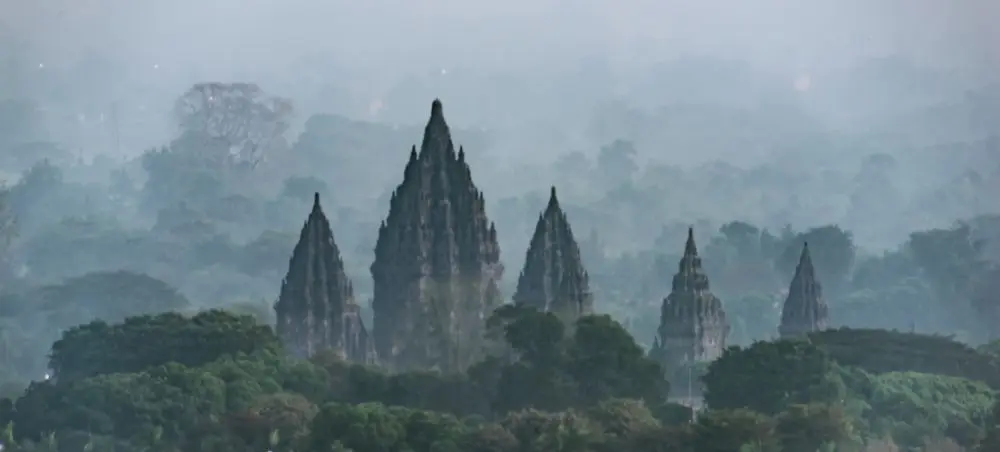 Ancient Prambanan temple complex rising through misty tropical forest near Yogyakarta, Indonesia